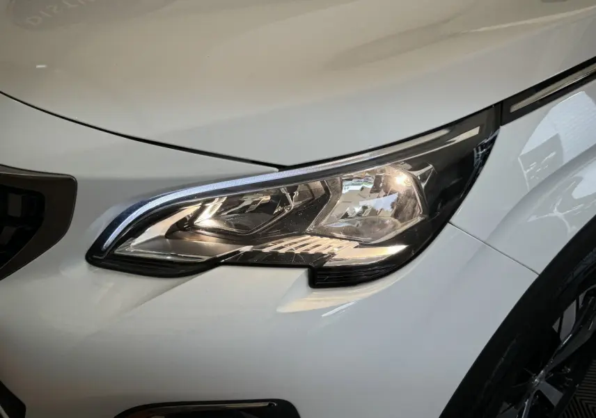 Gros plan sur le phare avant droit allumé du Peugeot 3008 blanc, soulignant les détails modernes du design.