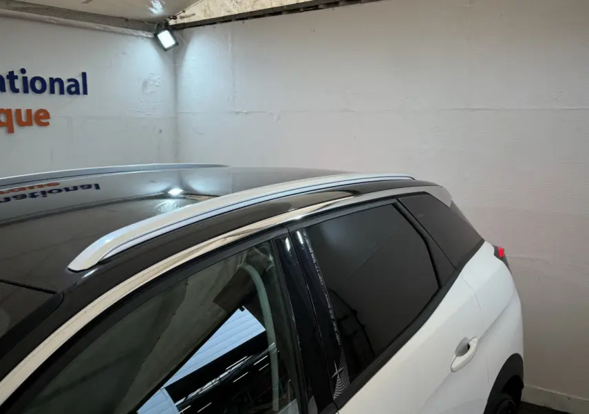 Vue latérale droite du Peugeot 3008 blanc avec toit noir et barres de toit chromées en intérieur fermé