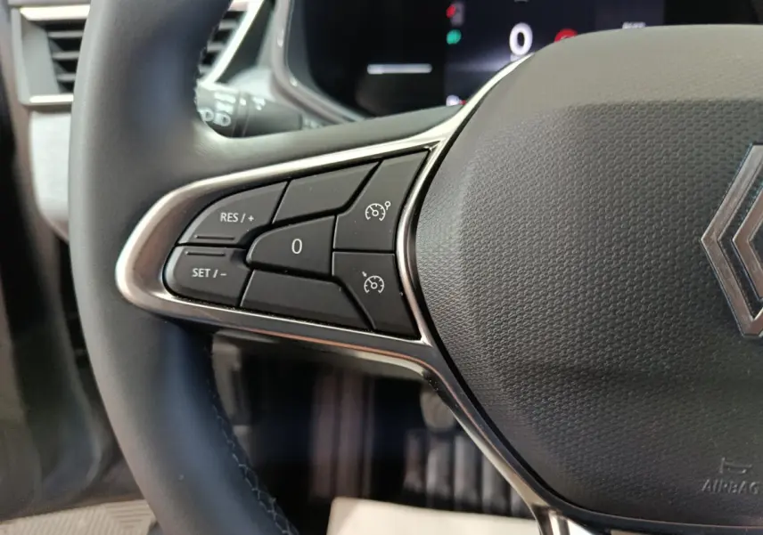 Gros plan sur le volant cuir synthétique de la Renault Clio gris foncé, avec commandes de régulateur de vitesse visibles à gauche.