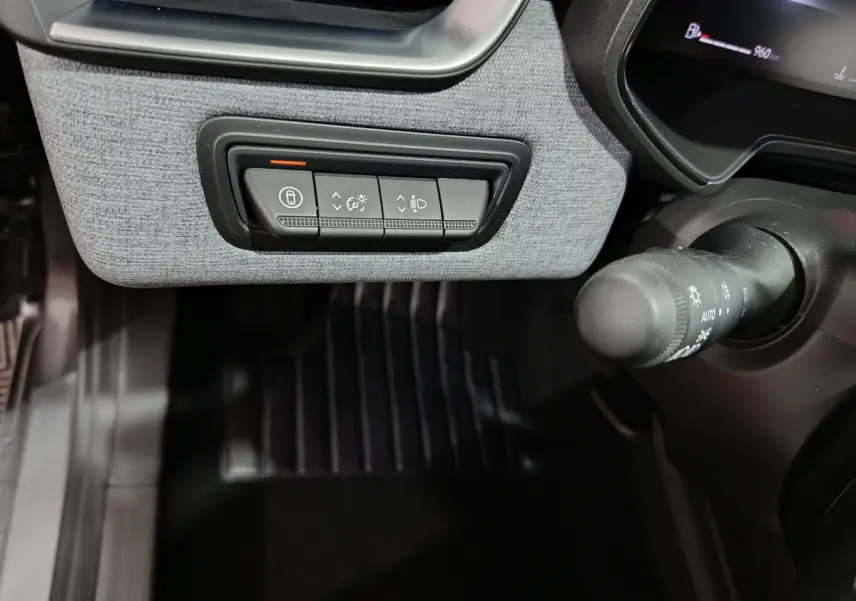 Gros plan sur les commandes d'éclairage et verrouillage sous le tableau de bord gris clair d'une Renault Clio 2025.