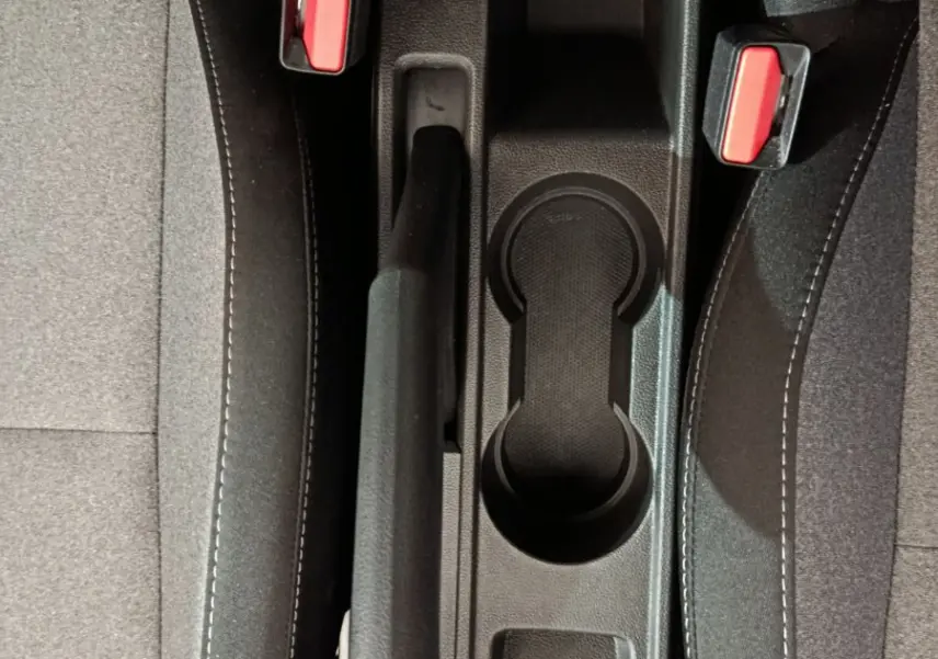 Vue plongeante sur la console centrale noire avec frein à main et ceintures rouges entre les sièges gris foncé Renault Clio 2025.