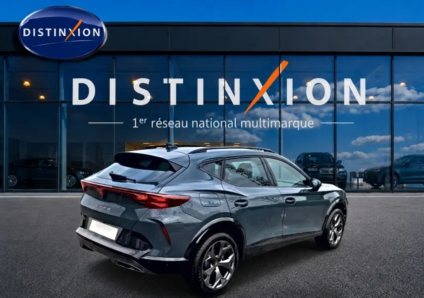 Vue 3/4 arrière droite du CUPRA Formentor 1.5 etsi hybrid bleu fjord avec jantes 18 pouces devant un showroom Distinxion.
