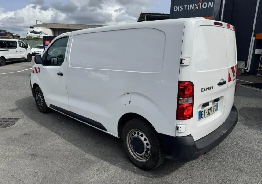 Vue 3/4 arrière droit d'un Peugeot Expert Fourgon blanc avec boucliers noirs et marquages rouges sur l'aile avant.