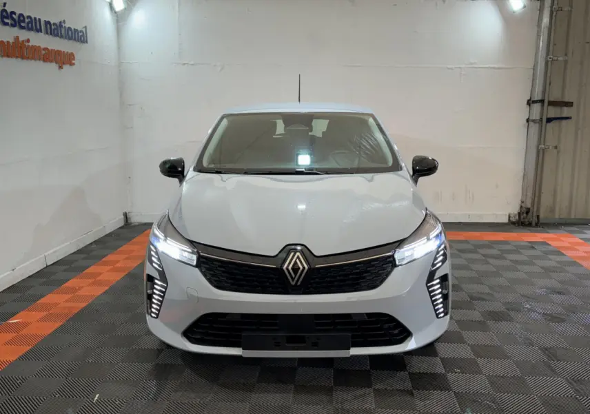 Vue frontale d'une Renault Clio gris clair 2025 avec feux LED allumés dans un garage.