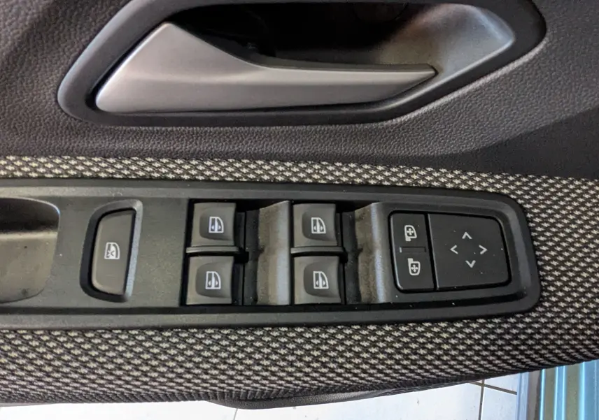 Gros plan sur les commandes des vitres électriques et réglages des rétroviseurs sur la porte côté conducteur du Dacia Jogger 2025.