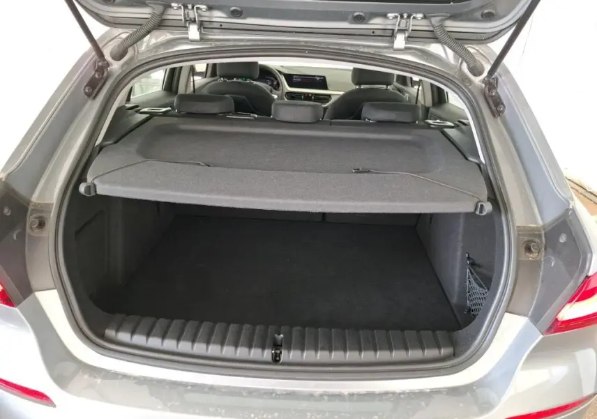 Coffre ouvert vu de l'arrière d'une BMW Série 1 116d gris 2022, avec cache-bagages et intérieur visible.