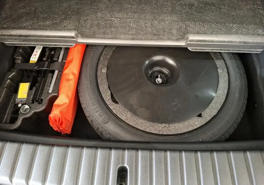 Coffre ouvert montrant la roue de secours et le kit de réparation dans une BMW Série 1 116d Business Design gris 2022.