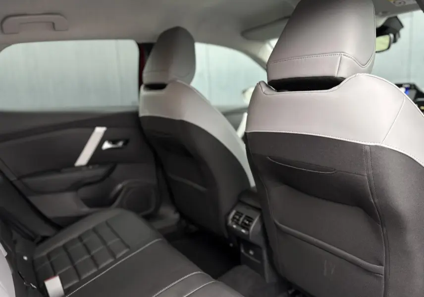 Vue intérieure arrière de la Citroën C4 Hybrid 2025 montrant les sièges bicolores gris clair et noir avec aérations centrales.