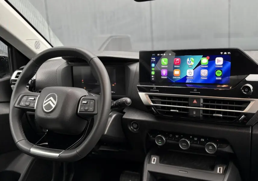 Vue intérieure du poste de conduite Citroën C4 Hybrid 2025, volant multifonction et écran tactile central lumineux.