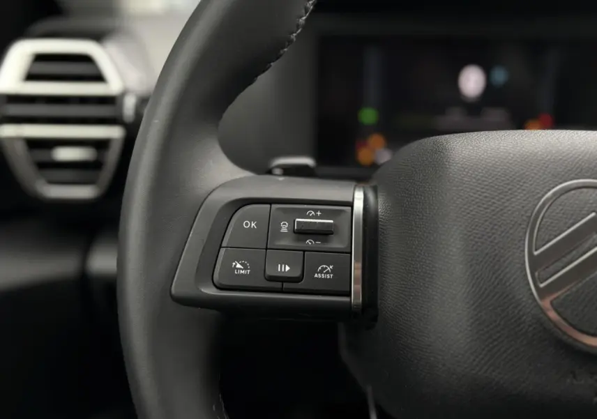 Gros plan sur les commandes au volant à gauche du Citroën C4 Hybrid 2025, cuir noir et logo Citroën visible.