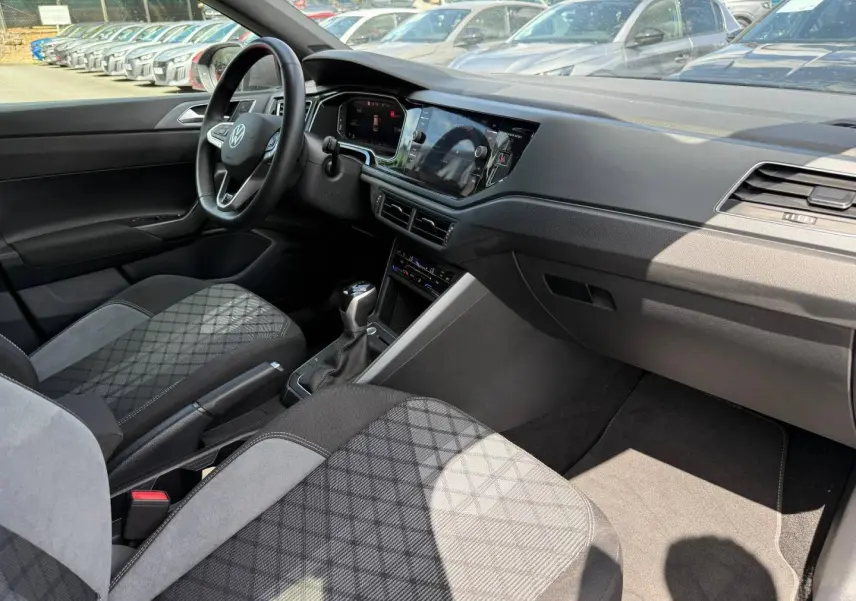 Vue intérieure côté conducteur du Volkswagen Taigo 2025, sièges tissu R-Line gris et tableau de bord moderne avec écran tactile.