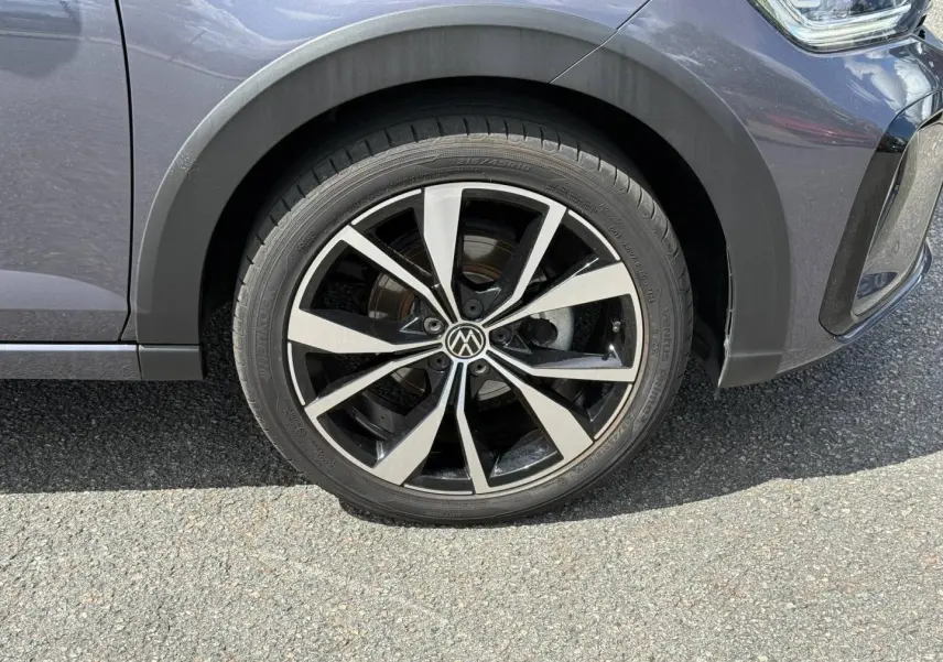Gros plan sur la roue avant gauche du Volkswagen Taigo gris avec jante alliage noir et argentée en étoile.