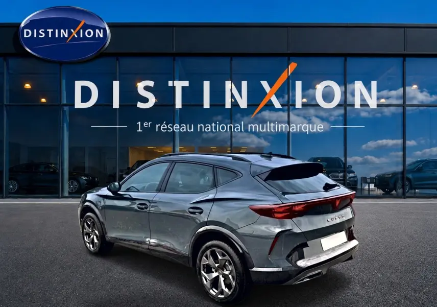 Vue 3/4 arrière droite d'un CUPRA Formentor bleu fjord avec feux arrière LED et jantes alliage devant un showroom Distinxion.