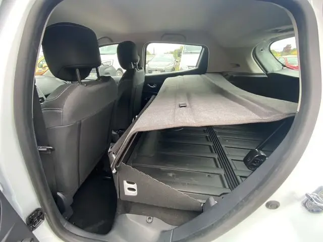 Vue intérieure arrière côté droit d'une Renault Clio IV blanche, montrant les sièges noirs et le coffre avec cache-bagages partiellement relevé.