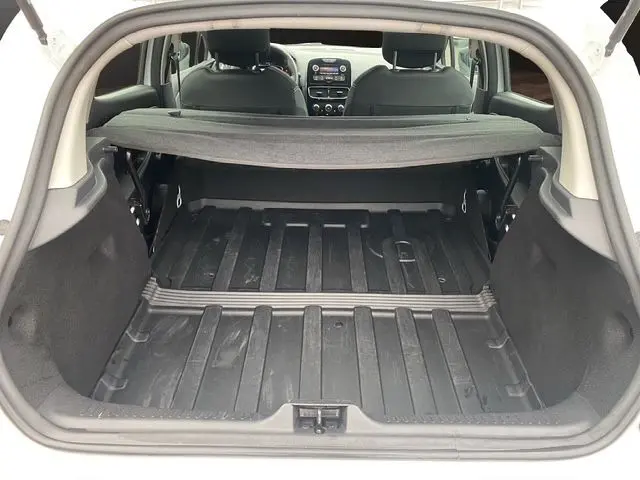 Vue depuis l'arrière du coffre vide d'une Renault Clio IV blanche, avec tablette cache-bagages et intérieur noir visible.