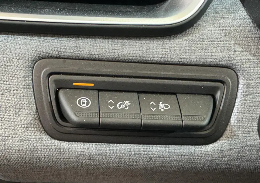 Gros plan sur les commandes de réglage des phares et verrouillage, sur le tableau de bord tissu gris de la Renault Clio 2025.
