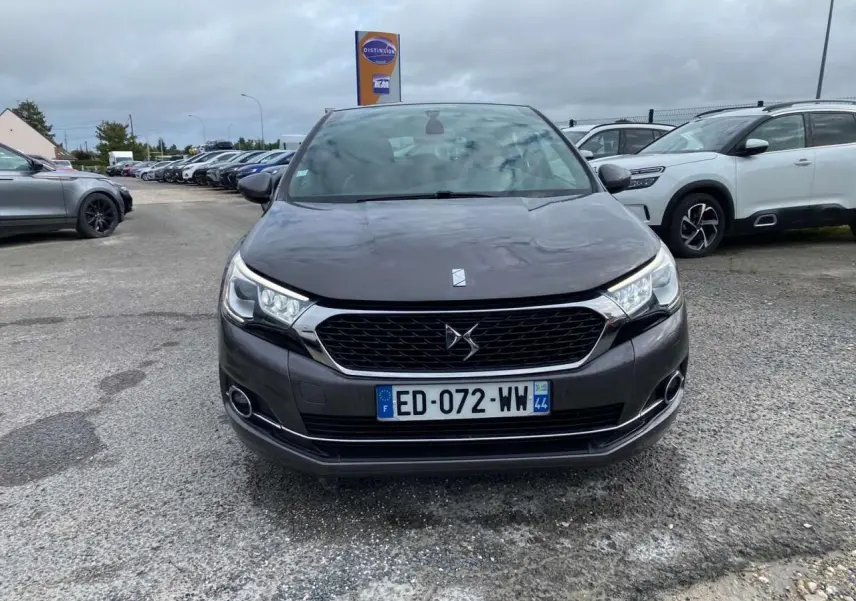 Vue avant d'une DS4 gris clair avec calandre noire et feux diurnes LED sur un parking extérieur.
