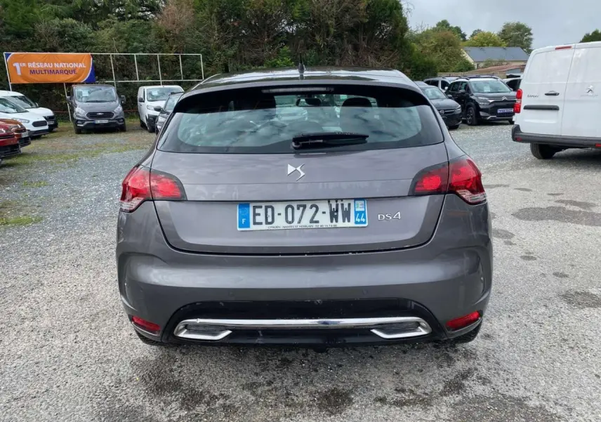 Vue arrière d'une DS4 gris clair avec feux rouges et double sortie d'échappement chromée sur un parking.