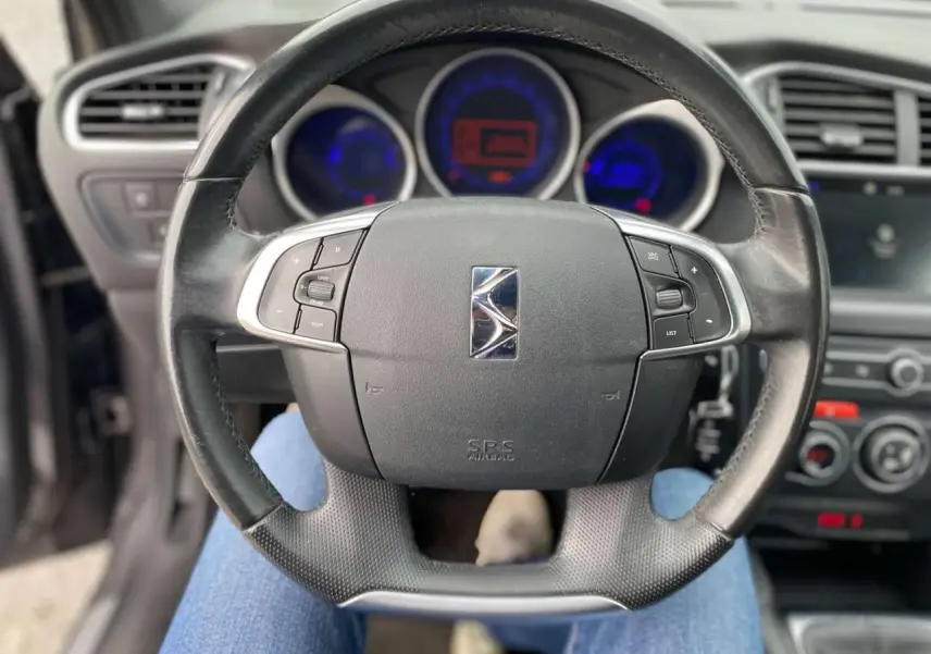 Vue rapprochée du volant noir du DS4 2016 avec commandes intégrées et tableau de bord lumineux en arrière-plan.