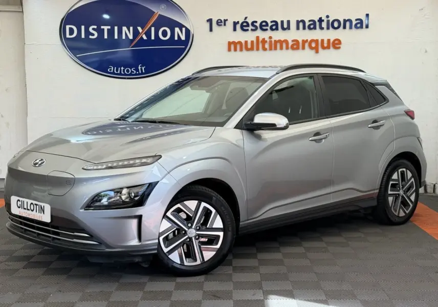 Vue 3/4 avant droite d'un Hyundai Kona électrique gris clair avec jantes spécifiques et rétroviseurs chromés.