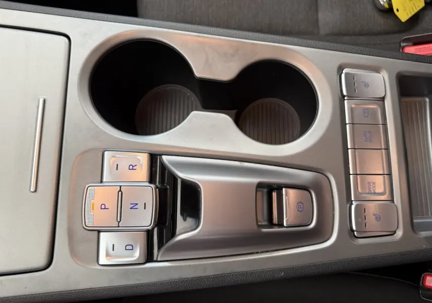 Gros plan sur la console centrale grise du Hyundai Kona électrique 2022 avec boutons de boîte auto et porte-gobelets.