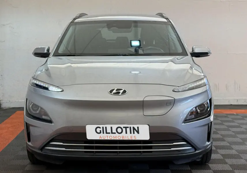 Vue de face du Hyundai Kona électrique gris clair avec phares LED et calandre épurée en intérieur showroom.