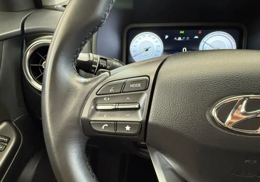 Gros plan sur le volant cuir noir du Hyundai Kona électrique 2022 avec commandes audio et tableau de bord numérique.
