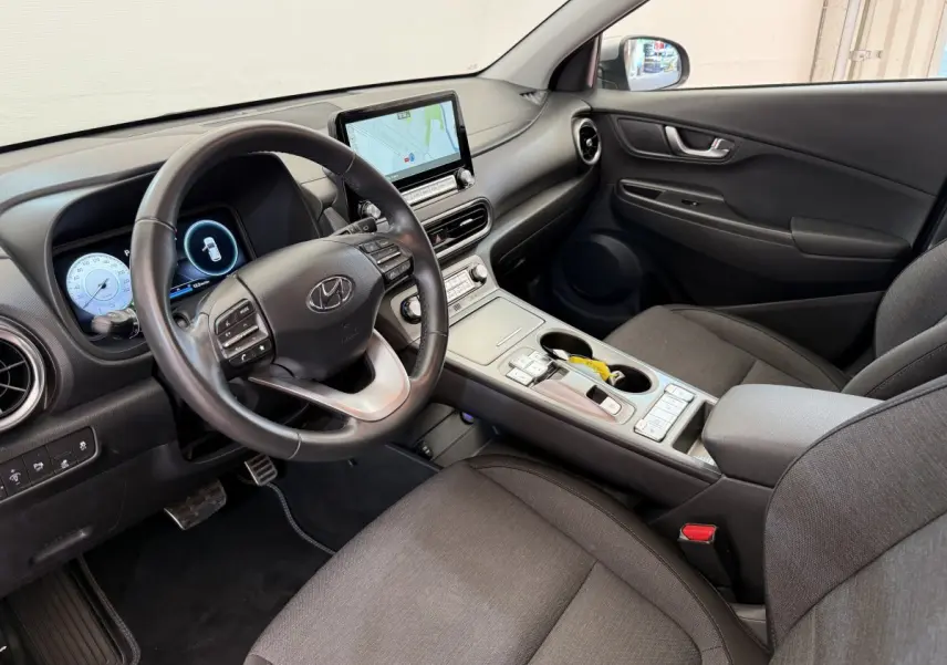 Intérieur côté conducteur du Hyundai Kona électrique 2022, tableau de bord noir avec écran tactile et volant cuir multifonctions.