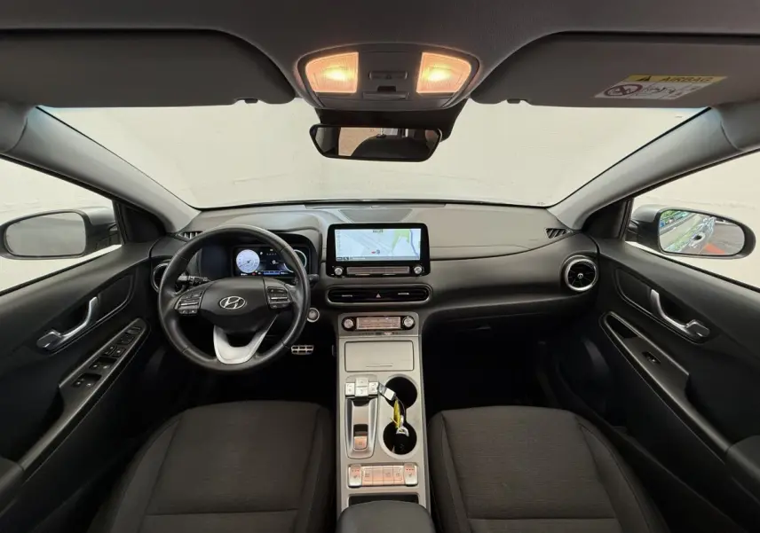 Vue intérieure avant du Hyundai Kona gris clair 2022, tableau de bord moderne avec écran tactile central et volant multifonctions cuir.