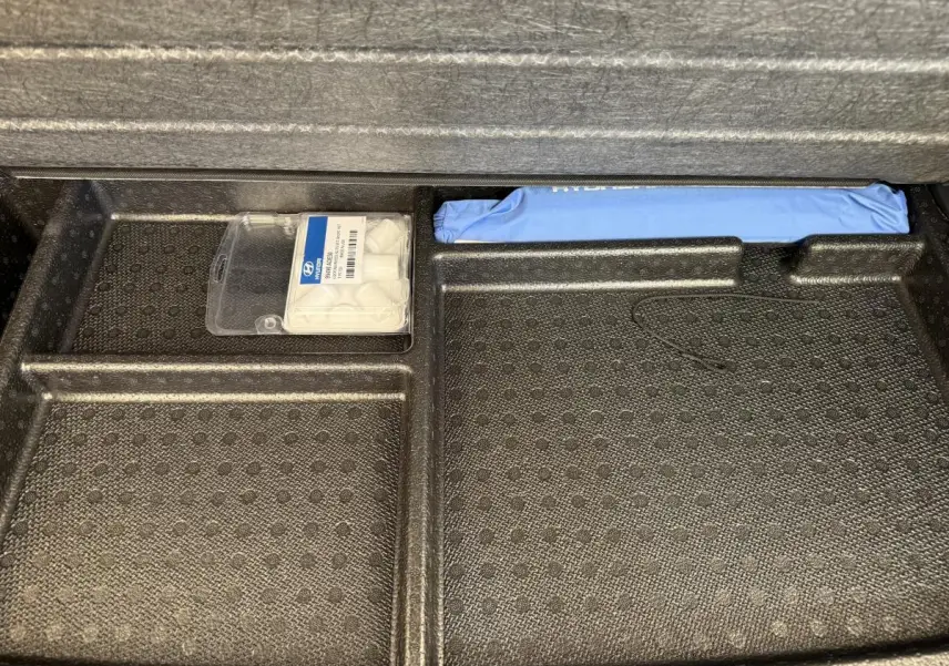 Rangement sous tablette de coffre Hyundai Kona gris clair 2022 avec kit de réparation pneus et trousse bleue.