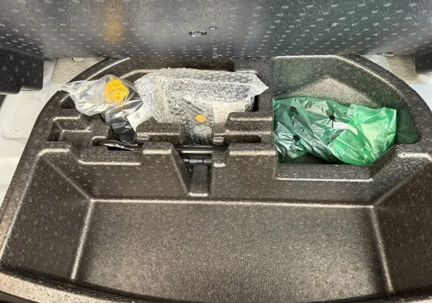 Compartiment de rangement sous le plancher du coffre du Hyundai Kona électrique gris clair, avec outils emballés visibles.