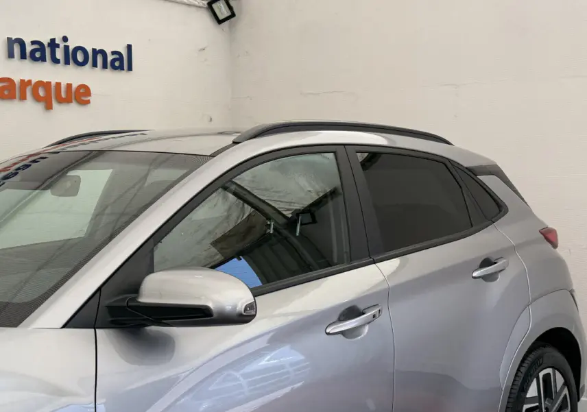 Vue côté gauche du Hyundai Kona électrique gris clair 2022, mettant en valeur les rétroviseurs et les poignées de porte chromées.