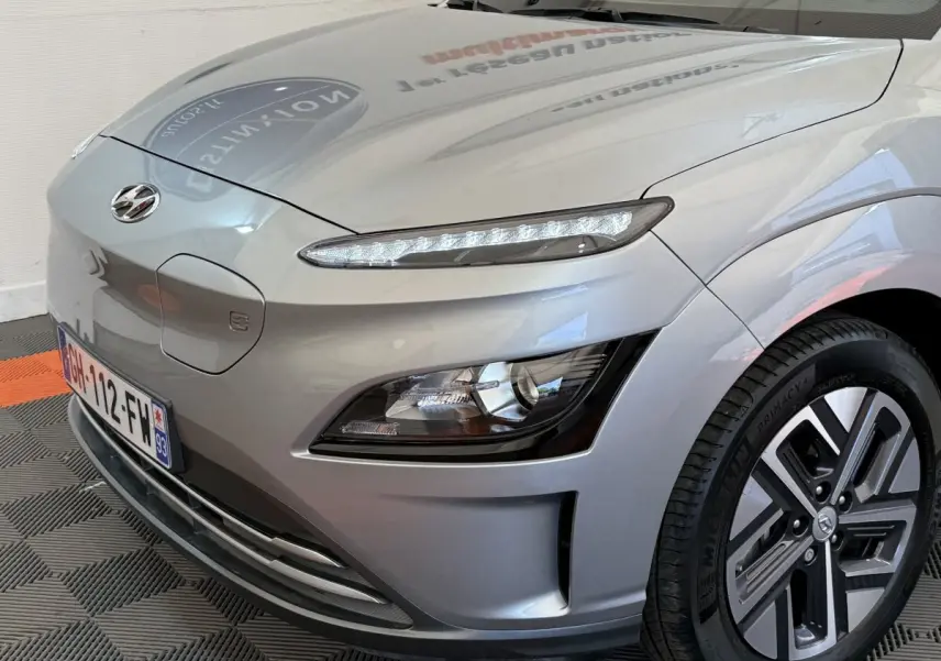 Vue 3/4 avant droit du Hyundai Kona gris clair électrique, mettant en valeur ses phares LED et jante spécifique.