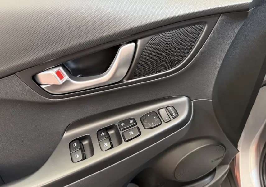 Gros plan sur la porte côté conducteur gris clair du Hyundai Kona électrique, montrant les commandes des vitres et le haut-parleur.