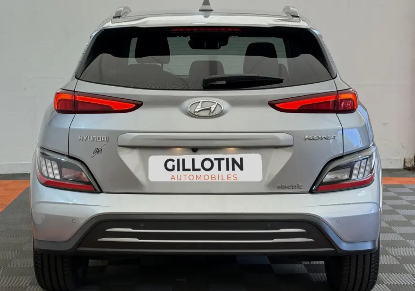 Vue arrière d'un Hyundai Kona électrique gris clair avec feux LED et logo "electric" visible sur le coffre.