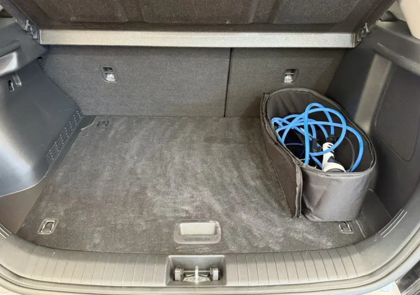 Coffre ouvert du Hyundai Kona électrique gris clair avec câble de recharge bleu rangé dans un sac noir.