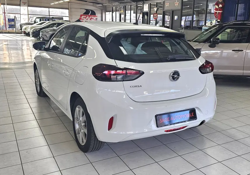 Vue 3/4 arrière d'une Opel Corsa blanche glacier 5 portes dans un showroom avec feux arrière foncés et toit noir.