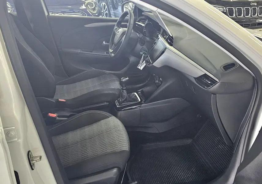 Vue intérieure côté conducteur de l'Opel Corsa blanc glacier 2022, montrant sièges tissu gris et tableau de bord moderne.
