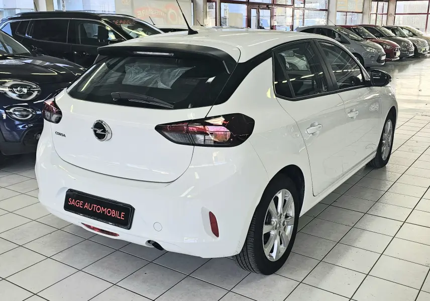 Vue 3/4 arrière droite d'une Opel Corsa blanche glacier 5 portes, avec feux arrière foncés et jantes alliage en showroom.