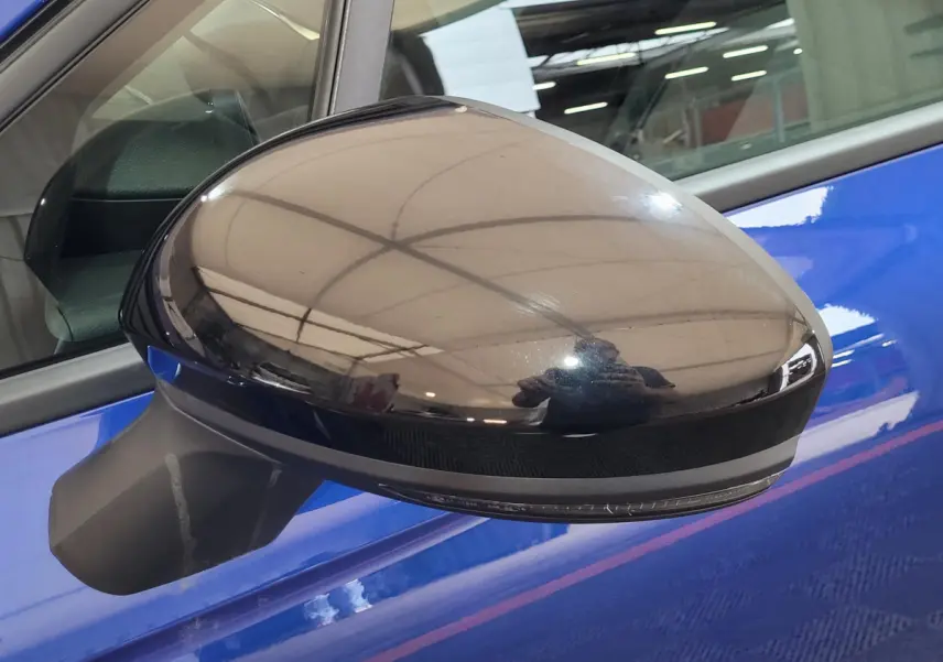 Rétroviseur côté gauche noir brillant sur Renault Clio bleu, avec reflet intérieur d'un garage.