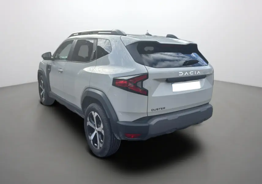 Vue 3/4 arrière gauche d'un Dacia Duster 2025 couleur Sandstone avec jantes alu 18 pouces et barres de toit.