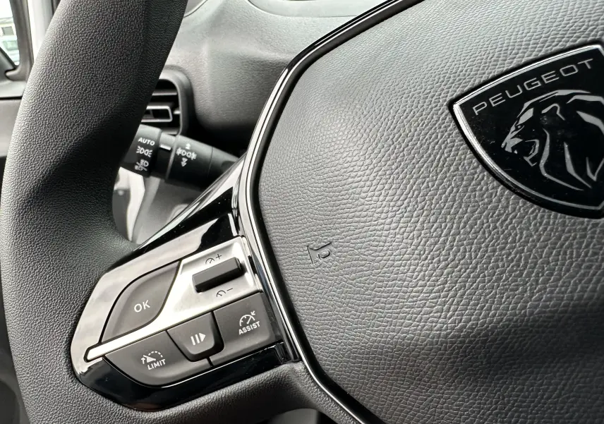 Gros plan sur le volant noir du Peugeot Partner Fourgon 2024 avec commandes intégrées et logo lion visible.