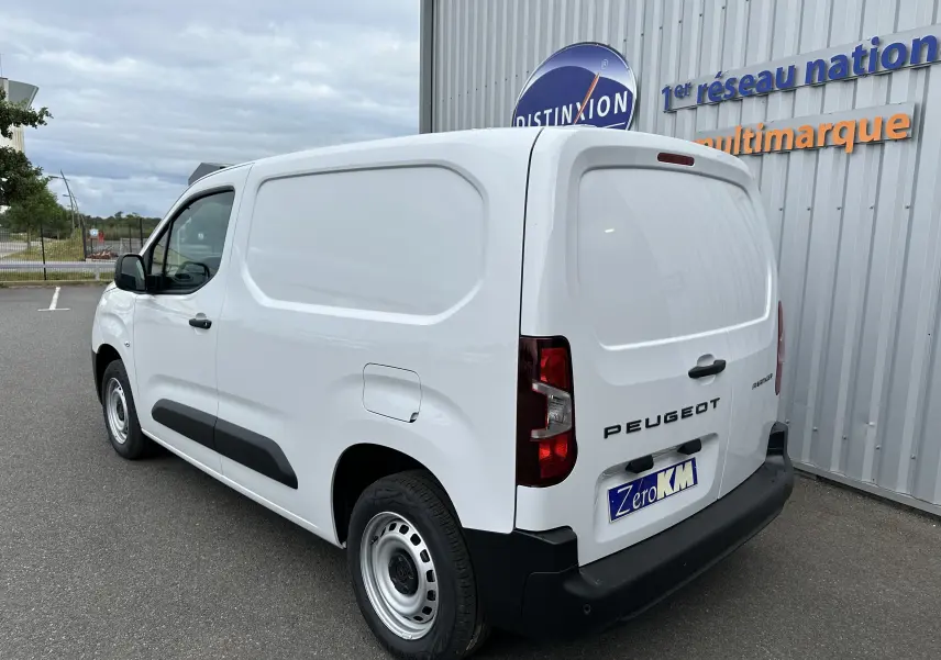 Vue 3/4 arrière droite d'un Peugeot Partner Fourgon blanc 2024 stationné devant un bâtiment commercial.