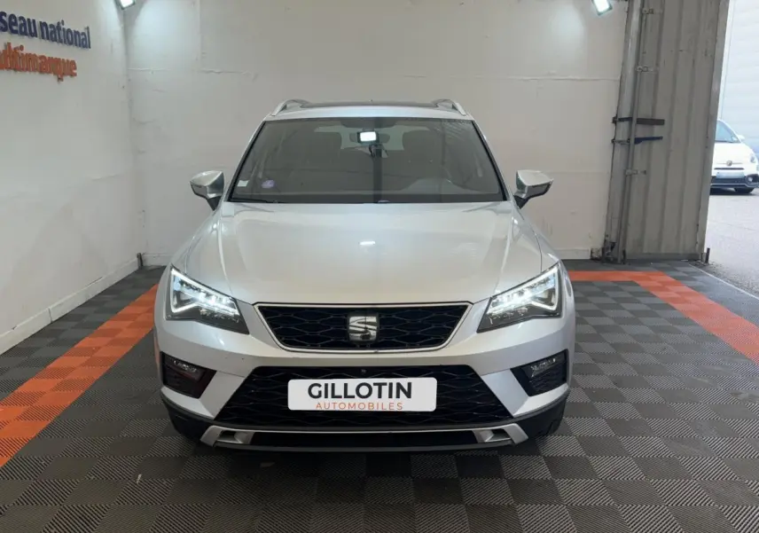 SEAT Ateca gris clair vu de face, phares LED allumés, calandre noire et toit avec barres de toit visibles.