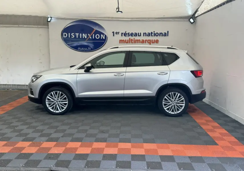 Profil côté gauche d'un SUV SEAT Ateca gris clair 2019 dans un showroom avec sol à damier gris et orange.