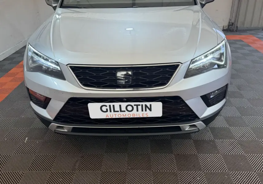 Vue frontale d'un SEAT Ateca gris clair avec phares LED allumés et calandre noire en intérieur showroom.
