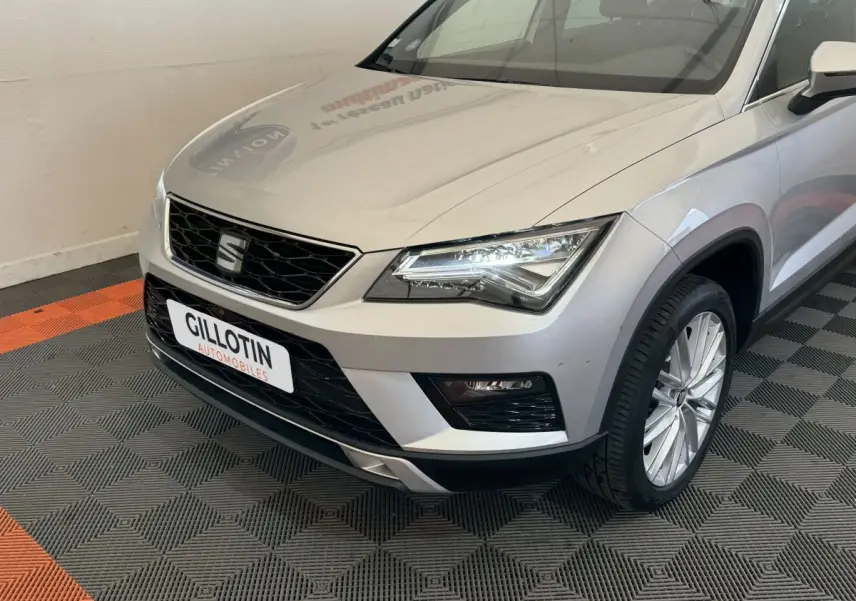 Vue 3/4 avant droit d'un SEAT Ateca gris clair avec phares LED et calandre noire en intérieur showroom.