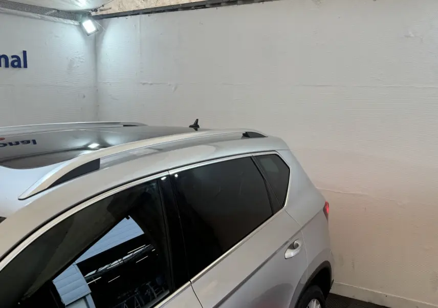 Vue côté droit arrière d'un SUV SEAT Ateca gris clair avec barres de toit et vitres teintées dans un garage.