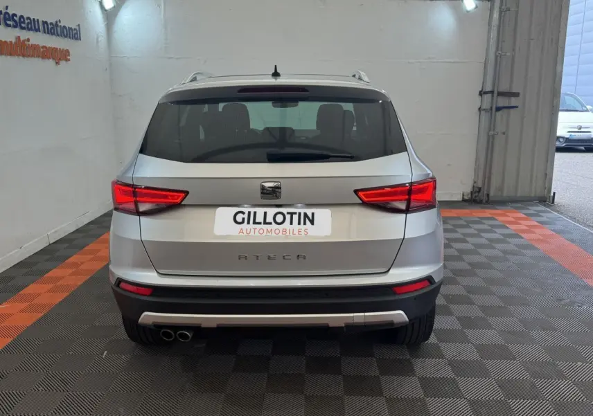 Vue arrière d'un SEAT Ateca gris clair stationné en intérieur avec feux arrière allumés et double sortie d'échappement visible.