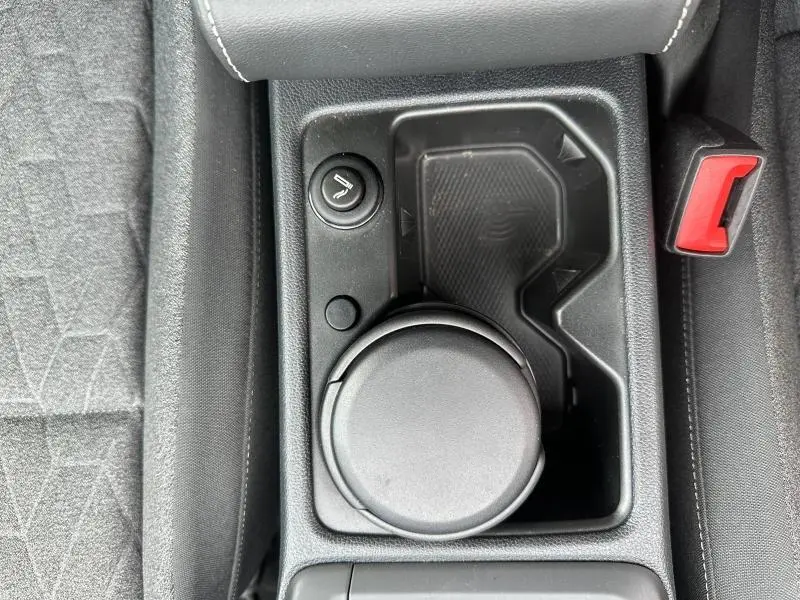 Vue plongeante sur la console centrale noire avec porte-gobelets, bouton de chauffage de siège et ceinture rouge visible côté droit.